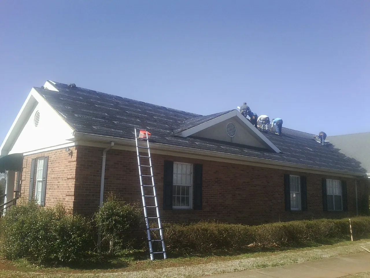 Crew tearing shingles off a brick ranch roof with a ladder set — Emergency Roof Repair work by our crew in Clay Center