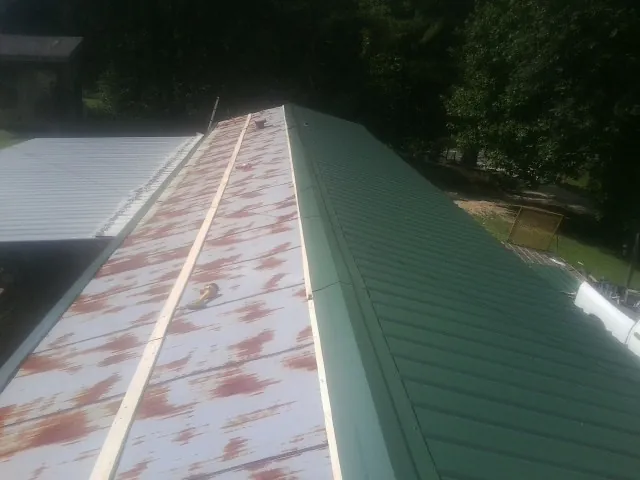 Old rusted panels beside newly installed green metal roofing — Wind Damage Roof Repair by Roofing Brothers in Clay Center