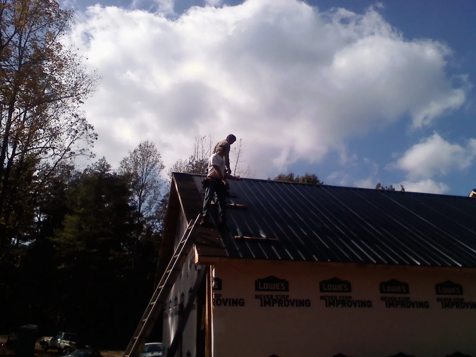 Roofer fastening dark metal panels high against a cloudy sky, from a Roof Inspection job in Clay Center
