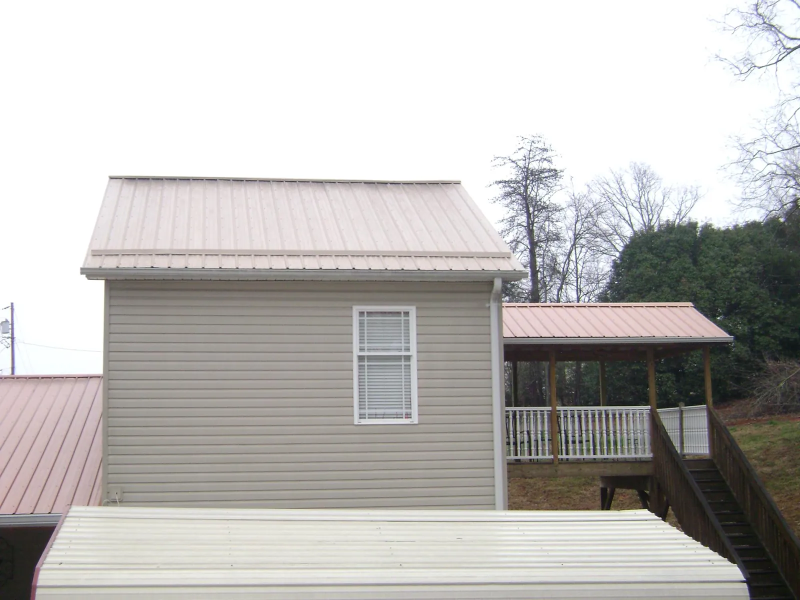 Tan metal roofs on a two story addition and attached porch, from a Roof Replacement job in Clay Center